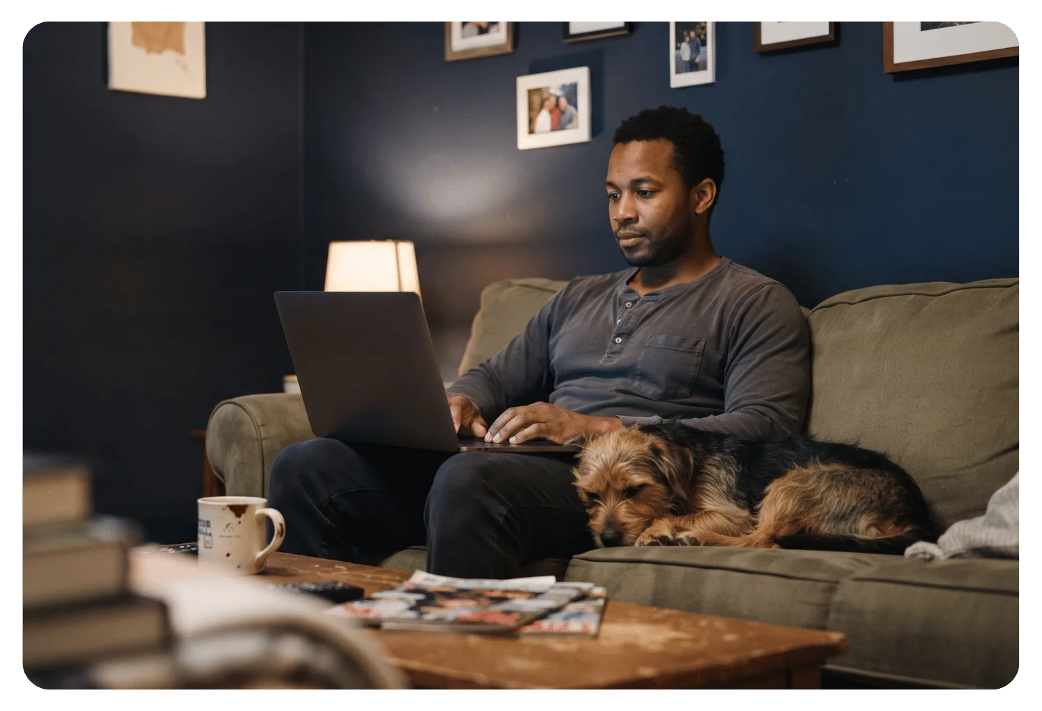 Business owner working on a laptop from his couch at home while his scruffy dog sleeps beside him