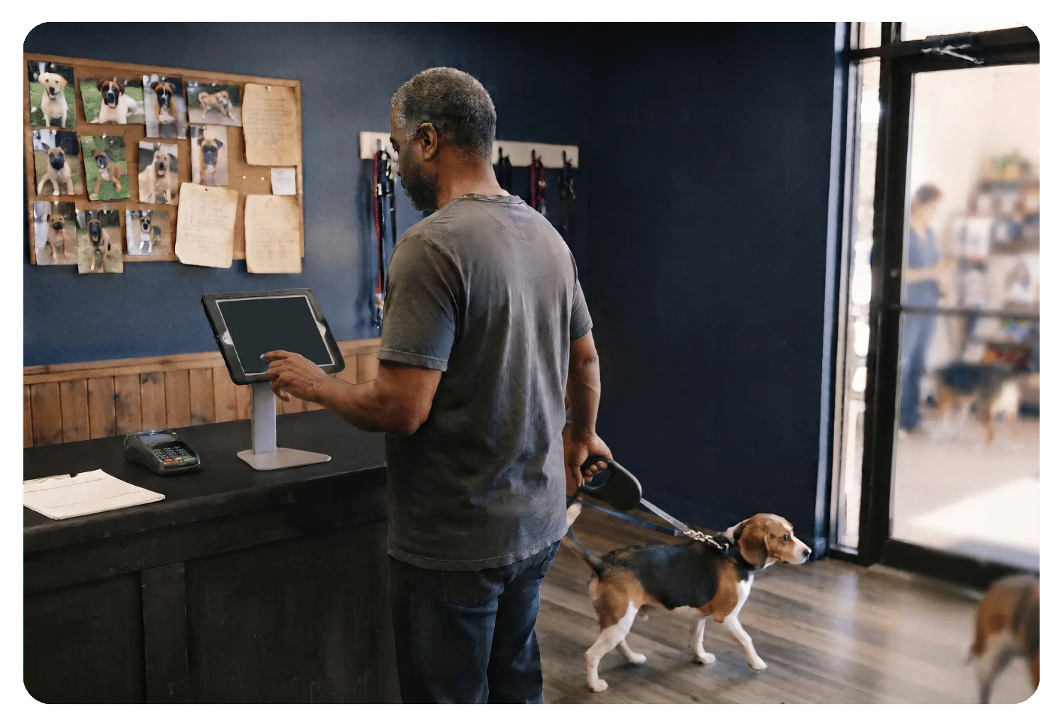 Pet parent checking in on a tablet kiosk at the front counter while holding his beagle on a leash
