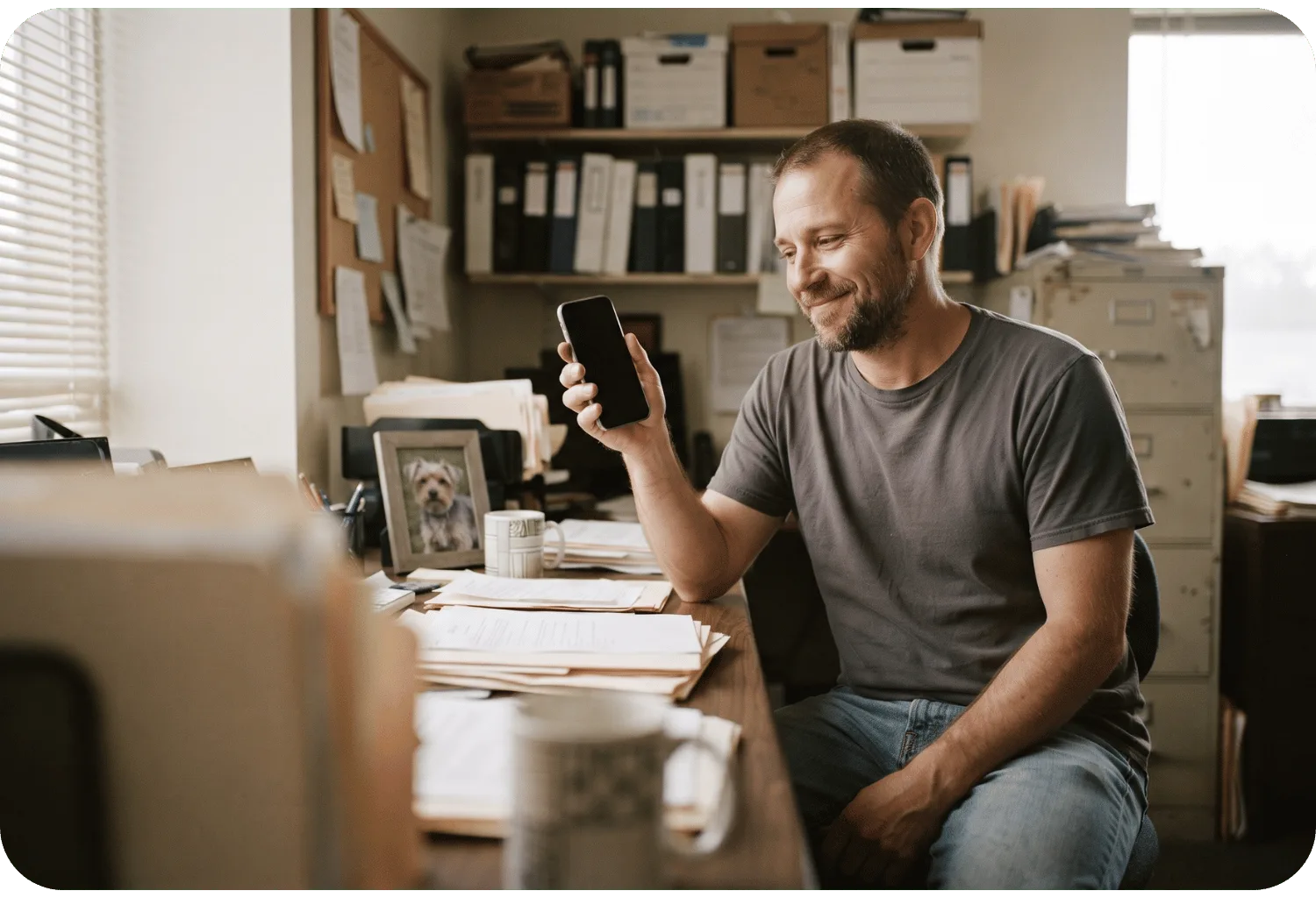 Pet parent smiling at his phone at his office desk, with a framed photo of his dog beside him