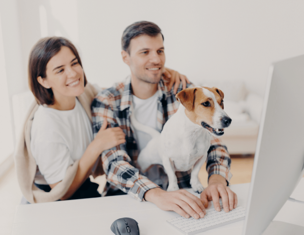 A couple sits at a desk with a computer, while a dog stands on the desk, curiously eyeing the screen as automated reminders pop up on TAB.