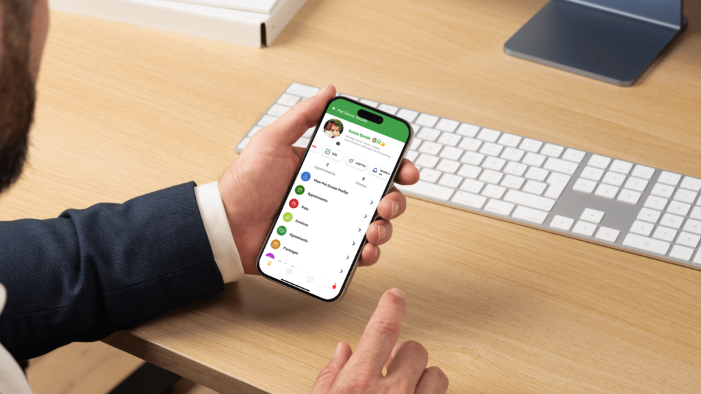 A person in a suit holds a smartphone displaying a messaging app interface at a desk with a computer keyboard and monitor, perhaps discussing ideas for the Scent Room.